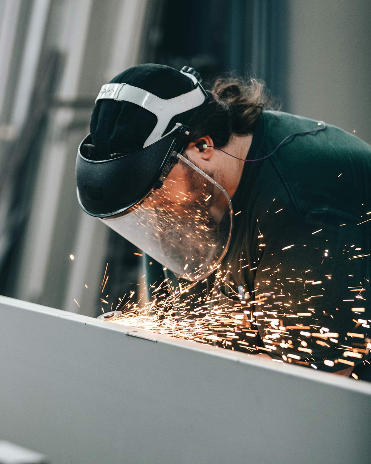 A fabricator in a welding hood grinding the edge of a sheet metal panel